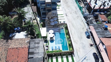 Vista aérea de un hotel con piscina, un espacio al aire libre cubierto y una calle con coches estacionados.