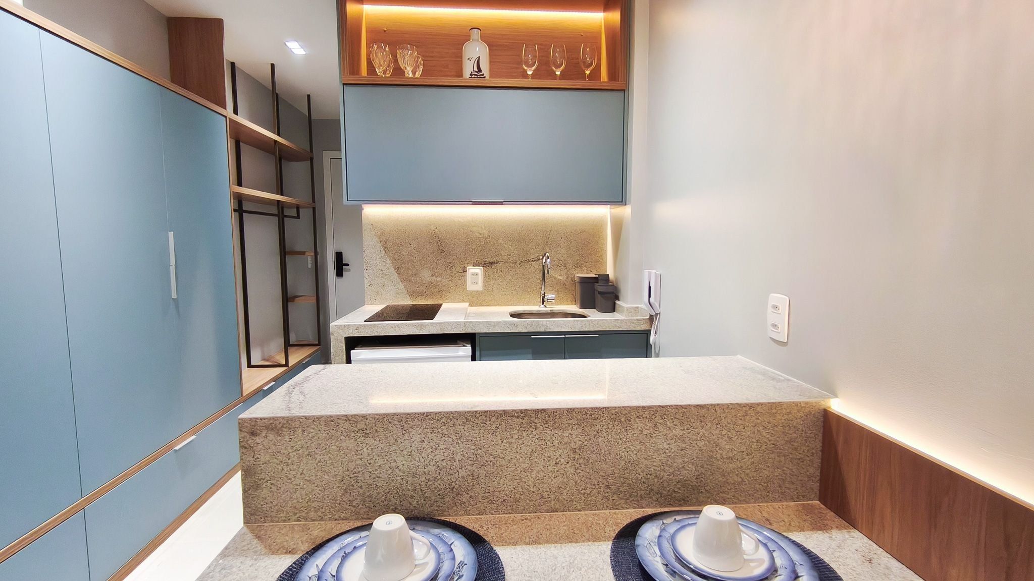 Une salle de bain moderne avec un comptoir en granit, un lavabo et un miroir. On y trouve des armoires et une étagère où sont disposés des objets décoratifs.