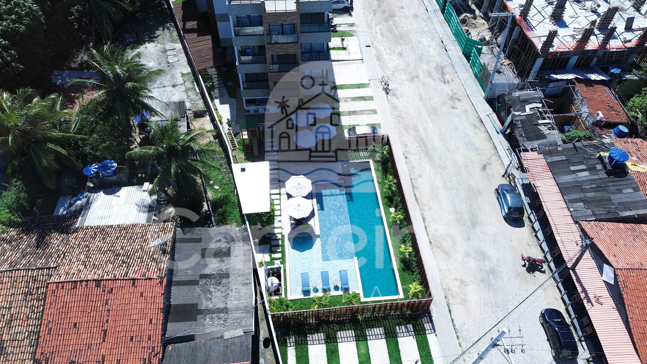 An aerial view of a hotel with a swimming pool, a covered outdoor area, and a street with parked cars.