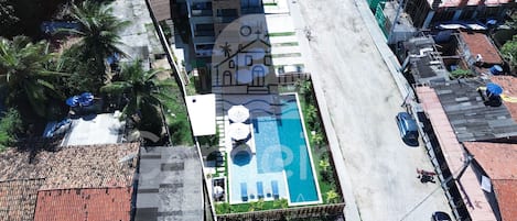 An aerial view of a hotel with a swimming pool, a covered outdoor area, and a street with parked cars.