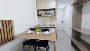 A compact kitchen with a microwave, sink, and cabinets. There is a dining table with chairs and a small potted plant. - Maré Alta Beach Hall-Praia de Tamandaré (Tamandaré)
