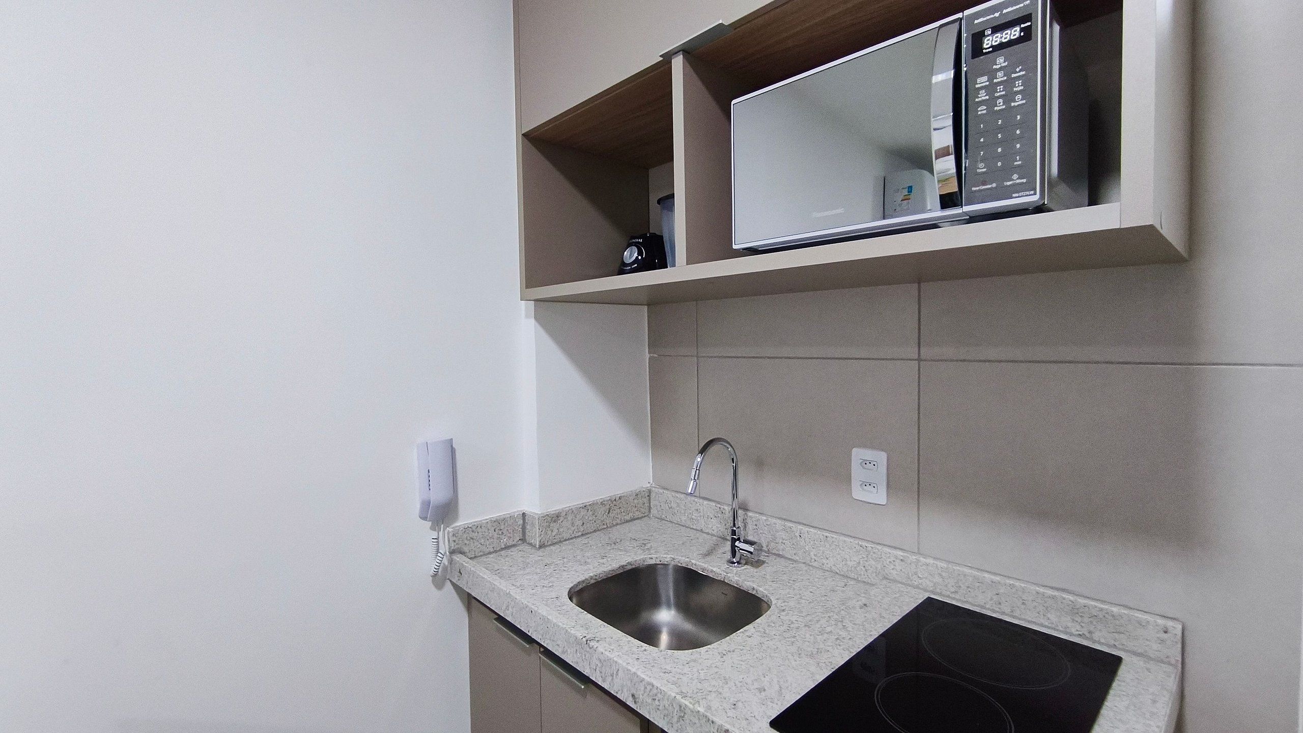 A kitchen with a granite countertop, stainless steel sink, and a microwave above it.