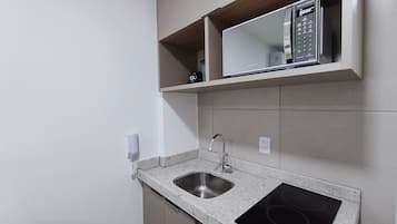A kitchen with a granite countertop, stainless steel sink, and a microwave above it.