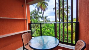 A balcony with a round table and two wicker chairs, overlooking lush greenery and palm trees. - Maré Alta Beach Hall-Praia de Tamandaré (Tamandaré)