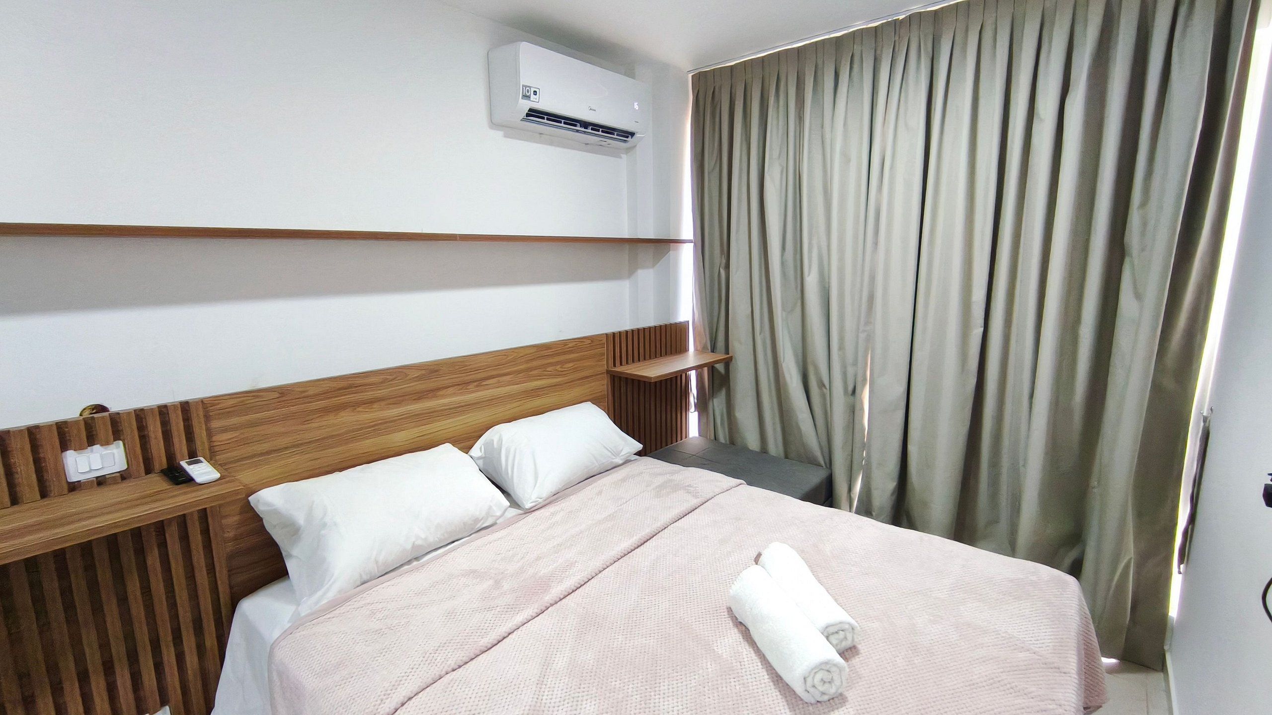 Une chambre d’hôtel comprenant un lit, une table de chevet, une commode, un climatiseur fixé au mur et un rideau.