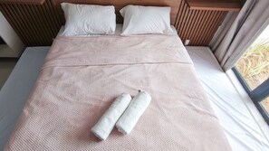 Ein Bett mit einer rosafarbenen, strukturierten Tagesdecke, zwei aufgerollten Handtüchern und weißen Kissen.