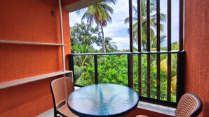 Ein Balkon mit einem runden Tisch und zwei Korbstühlen, mit Blick auf üppiges Grün und Palmen.