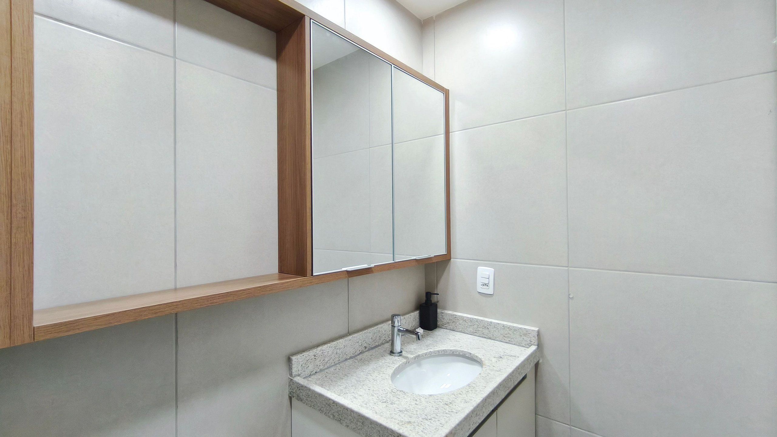 Un baño con lavamanos, espejo y paredes de azulejos.