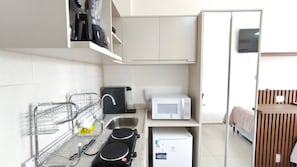 A compact kitchen with a microwave, kettle, and a small refrigerator.