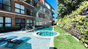 Un edificio moderno con piscina, mobiliario de exterior y un jardín bien cuidado.