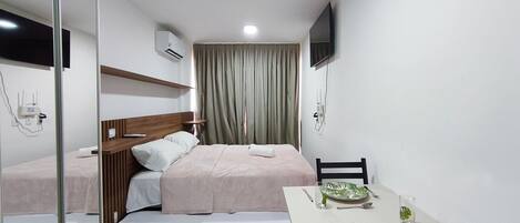 Une chambre d’hôtel avec un lit, une table de chevet sur laquelle se trouve un verre d’eau, une chaise et un téléviseur fixé au mur.