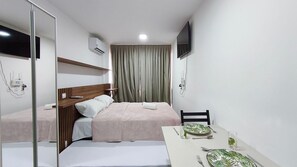 A hotel room with a bed, a bedside table with a glass of water, a chair, and a television mounted on the wall. - Maré Alta Beach Hall-Praia de Tamandaré (Tamandaré)