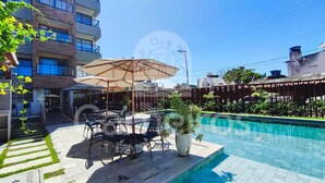 A swimming pool with a patio area, outdoor seating, and a building in the background. - Maré Alta Beach Hall-Praia de Tamandaré (Tamandaré)