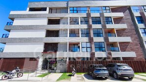 Un edificio de varios pisos con un diseño arquitectónico moderno, que combina fachadas de ladrillo y vidrio, y una entrada con puerta de acceso y vehículos estacionados.