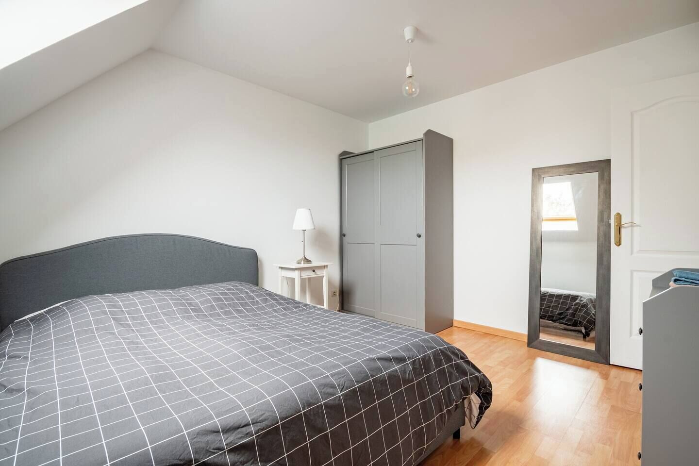 Een slaapkamer met een bed, een nachtkastje, een kledingkast en een deur naar een andere kamer.