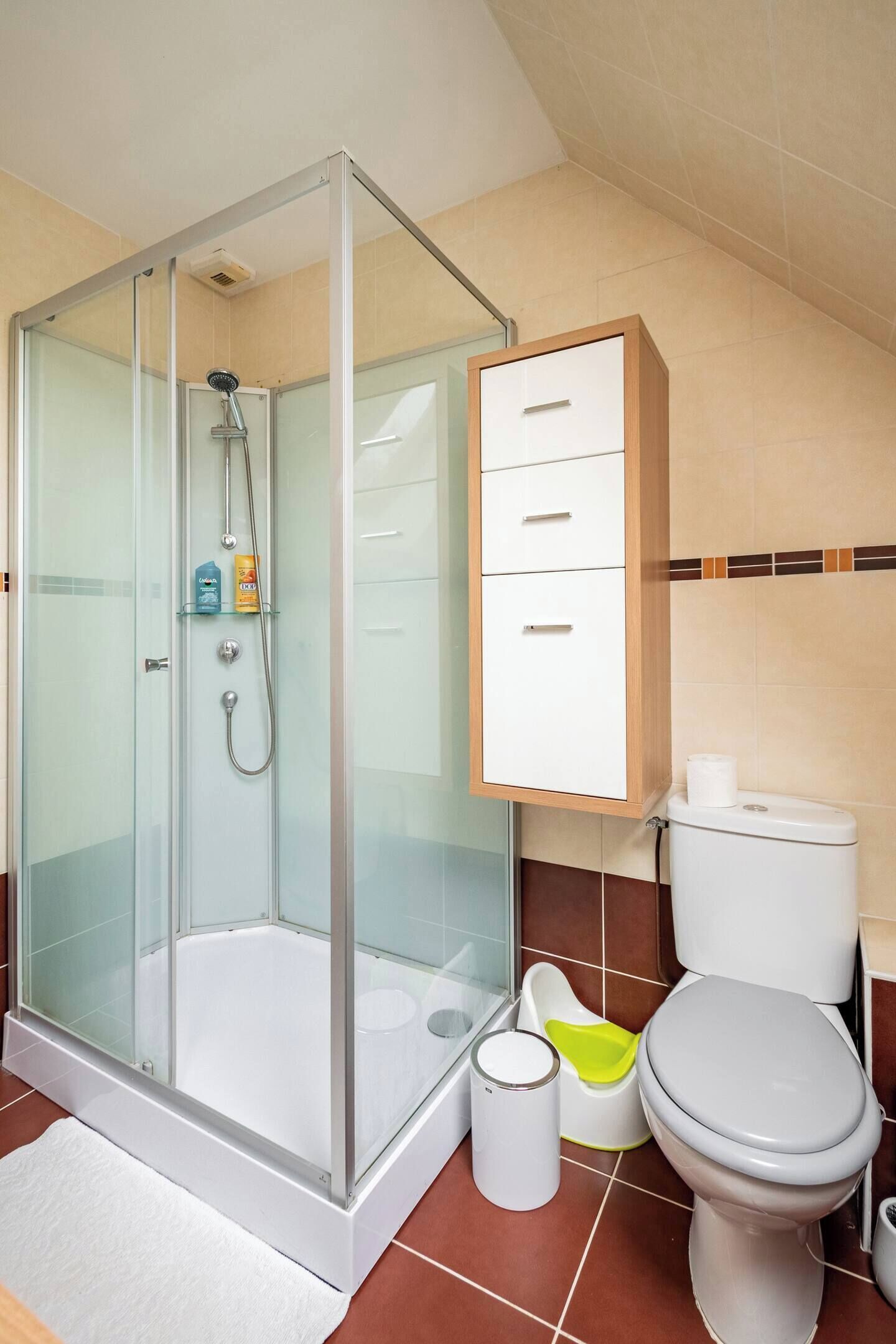 Un baño moderno con ducha envuelta en vidrio, un inodoro con reposapiés y un mueble con cajones.