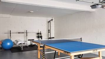 A ping pong table in a room with a white wall, a blue exercise ball, and weightlifting equipment.