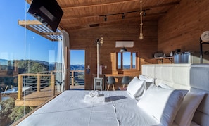Une cabane en bois avec un lit, une table, des chaises, un poêle et une vue sur les montagnes.