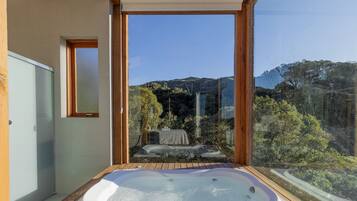 A bathroom with a hot tub, wooden flooring, and a view of a mountainous landscape.