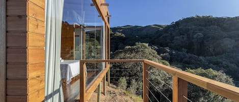 A wooden deck with a glass balustrade overlooking a forested hillside.