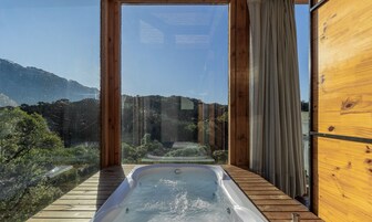 Una cabaña de madera con hidromasaje y vistas a un paisaje montañoso.