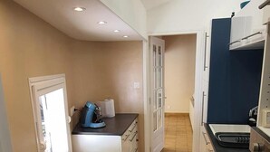 A narrow kitchen with a tiled floor, a trash bin, and a window. - Charming, renovated, air-conditioned single-storey house on the edge of a forest. (Saint-Jean-de-Monts)