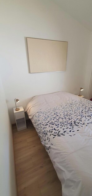 Ein Schlafzimmer mit einem Bett, einem Nachttisch, einer Wandleuchte und Holzboden.