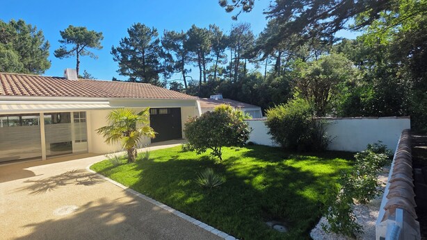 A modern house with a tiled roof, a covered patio, and a well-maintained lawn. - Charming, renovated, air-conditioned single-storey house on the edge of a forest. (Saint-Jean-de-Monts)