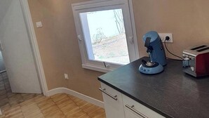 A kitchen with a window, a coffee machine, and a toaster on the counter. - Charming, renovated, air-conditioned single-storey house on the edge of a forest. (Saint-Jean-de-Monts)