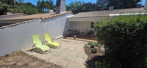 A patio with two yellow lounge chairs, a small table, and a seating area with chairs. - Charming, renovated, air-conditioned single-storey house on the edge of a forest. (Saint-Jean-de-Monts)