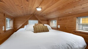 A bedroom with a large bed, wooden walls, and two windows with blinds. - Tiny Home 8- Mount Ethel (Bellvue)