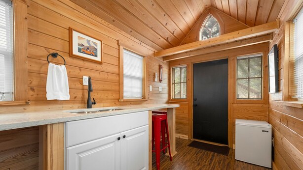 A compact kitchen with wooden walls, a white countertop, a red stool, and a small refrigerator. - Tiny Home 8- Mount Ethel (Bellvue)