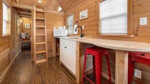 A compact wooden cabin with a kitchenette, a small seating area, and a ladder leading to a loft. - Tiny Home 8- Mount Ethel (Bellvue)