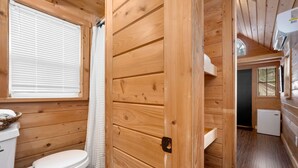 A wooden-paneled bathroom with a toilet, a sink, and a window with blinds. - Tiny Home 8- Mount Ethel (Bellvue)