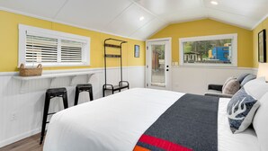 A bedroom with a bed, a window with blinds, a small table with a basket, and a door leading outside. - Cabin 2- Youngs Gulch (Bellvue)