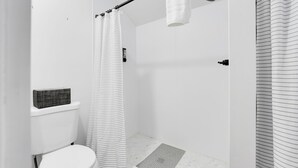 A bathroom with a shower, toilet, and a small shelf with a basket. - Cabin 2- Youngs Gulch (Bellvue)