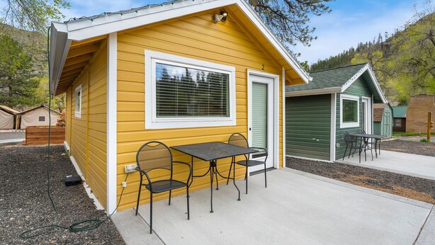 A yellow cabin with a patio table and chairs, a green door, and a small window. - Cabin 2- Youngs Gulch (Bellvue)
