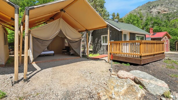 A rustic cabin with a covered outdoor seating area, a wooden deck, and a view of a mountainous landscape. - Glamp 17- Majestic Moose (Bellvue)