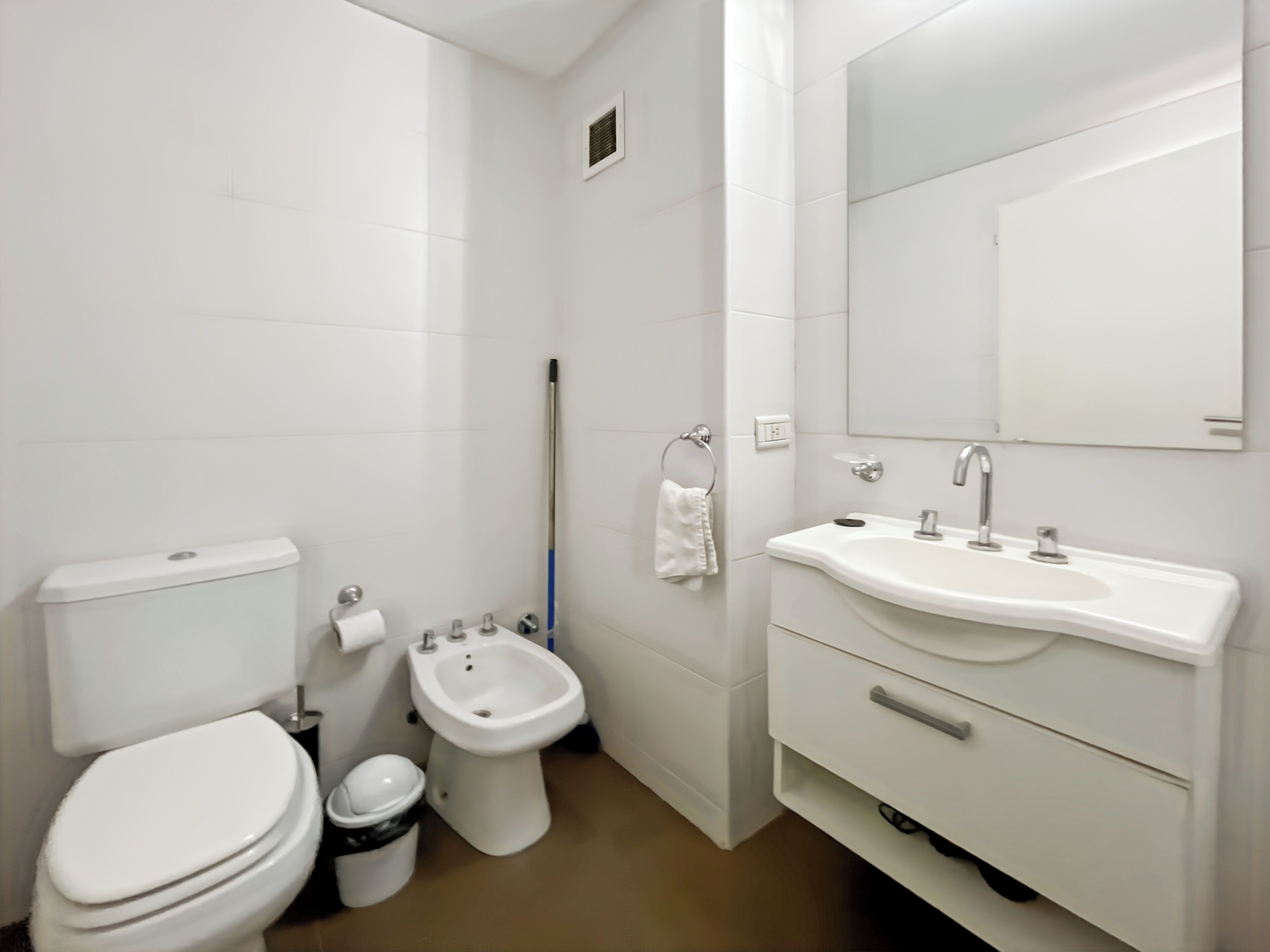 A modern bathroom with a toilet, bidet, sink, and mirror.