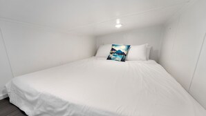 Camera con un letto singolo, biancheria bianca, cuscino a tema cielo stellato e una lampada a soffitto.