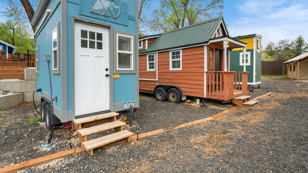 Un piccolo camper blu con una porta e finestre bianche, un portico e una rampa d'accesso alla porta.