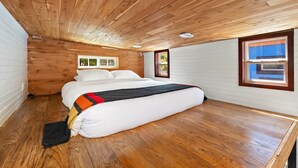 Ein Schlafzimmer mit Holzboden, einem Bett mit weißer Bettwäsche und zwei Fenstern.