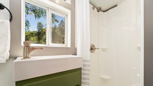 Ein Badezimmer mit weißem Waschbecken, einem grünen Schrank und einer Dusche mit einer weißen Tür.