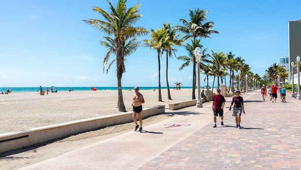 Eine Strandpromenade mit Palmen, wolkenlosem Himmel und einem sandigen Strand im Hintergrund.