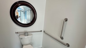 Ein kleines, modernes Badezimmer mit Toilette, rundem Spiegel und Handlauf.