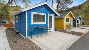 Eine blaue Holzhütte mit einer Terrassenanlage, inklusive Tisch und Stühlen, umgeben von Bäumen und einer hügeligen Landschaft.
