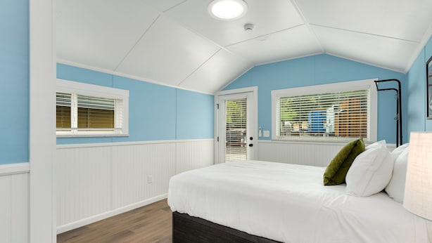 Ein Schlafzimmer mit einem großen Bett, weißer Bettwäsche, Holzboden und einem Fenster mit Jalousien.