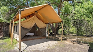 Una tenda amb un llit a l'interior, envoltada d'arbres i un riu.