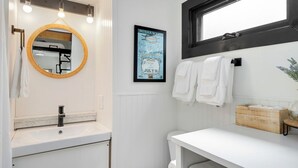 Un baño moderno con un espejo redondo, un lavabo blanco y un cartel en la pared.