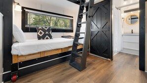 Un dormitorio pequeño con una cama nido, una escalera, una ventana con persianas y una puerta corredera que da a un baño.